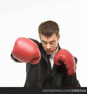 Caucasian mid-adult man wearing suit and punching with boxing gloves toward viewer.