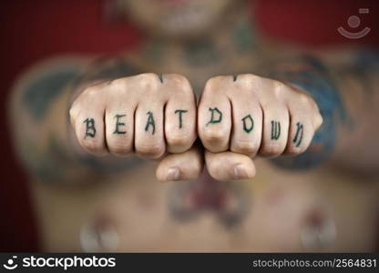 Caucasian mid-adult man with tattoos and piercings holding out fists reading beat down.