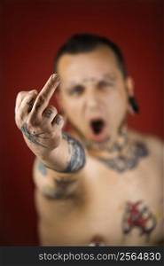 Caucasian mid-adult man with tattoos and piercings holding up middle finger.