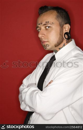 Caucasian mid-adult man with tattoos and piercings wearing necktie looking at viewer.