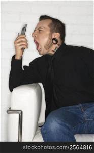 Caucasian mid-adult man with tattoos and piercings yelling into cell phone.