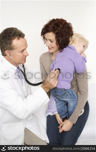 Caucasian mid-adult mother holding her female toddler while middle-aged male doctor uses stethoscope.