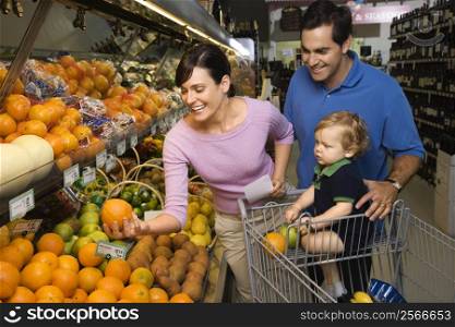 Caucasian mid-adult parents grocery shopping for fruit with male toddler.