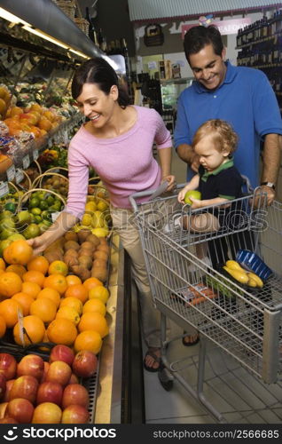 Caucasian mid-adult parents grocery shopping for fruit with male toddler.