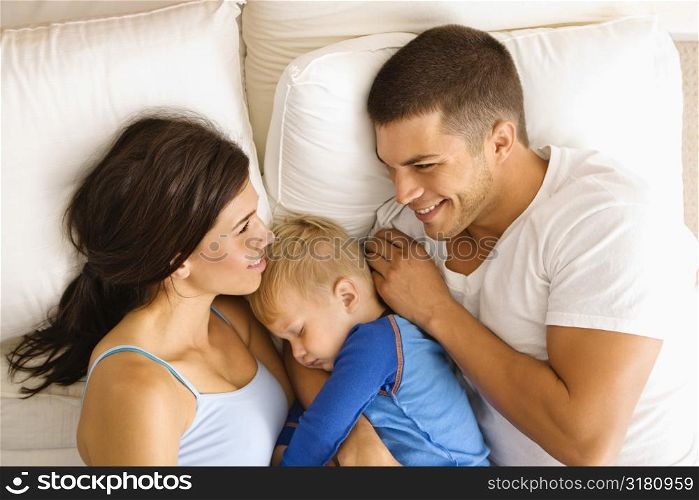 Caucasian mid adult parents with toddler son sleeping in bed.