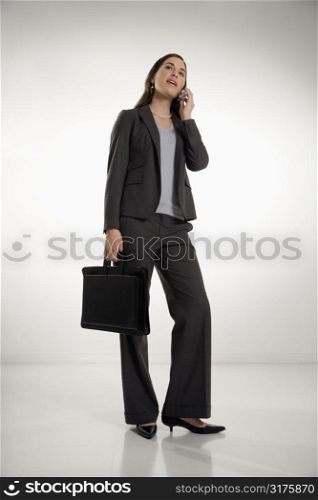 Caucasian mid adult professional business woman holding briefcase, talking on cell phone and smiling.