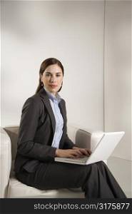 Caucasian mid adult professional business woman sitting in modern office working on laptop looking at viewer.