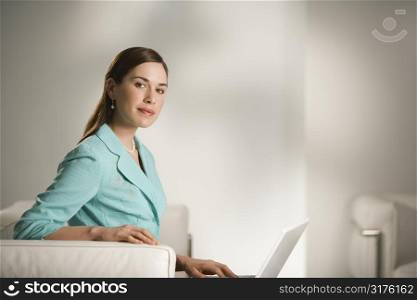 Caucasian mid adult professional business woman sitting in modern office working on laptop computer looking at viewer.