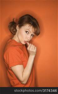 Caucasian mid-adult woman gesturing with thumb on orange background.