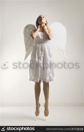 Caucasian mid-adult woman in white angel costume jumping in air.