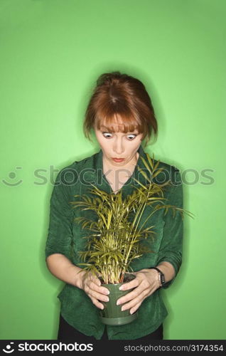 Caucasian mid-adult woman on green background looking at plant.