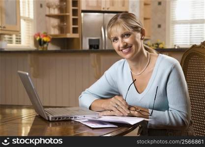 Caucasian mid-adult woman paying bills on laptop computer looking at viewer and smiling.