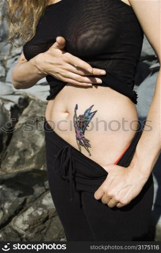Caucasian mid-adult woman revealing tattoo of fairy on stomach.