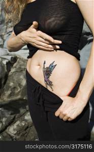 Caucasian mid-adult woman revealing tattoo of fairy on stomach.