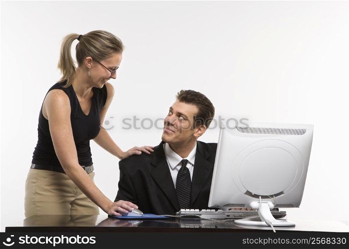 Caucasian mid-adult woman touching mid-adult man&acute;s shoulder and using mouse at computer.