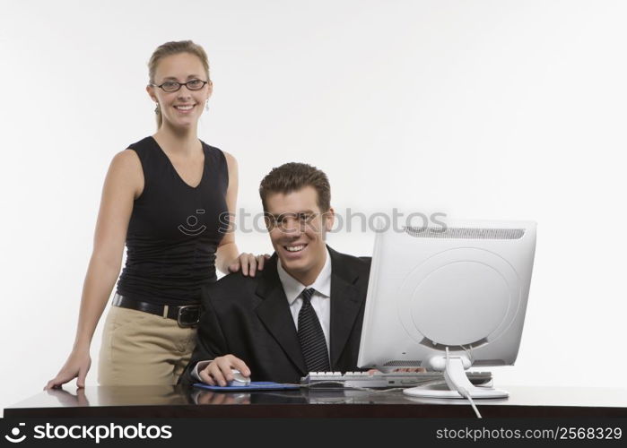 Caucasian mid-adult woman touching shoulder of man sitting at computer and looking at viewer.