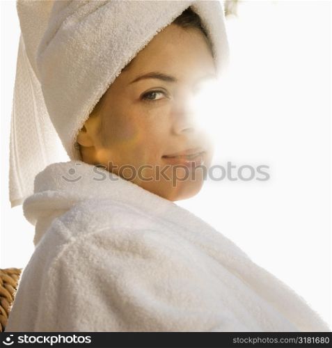 Caucasian mid-adult woman wearing robe and towel on head with sunlight behind her.