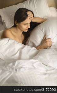 Caucasian mid-adult woman with hand on head in bed.