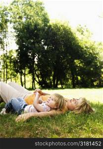 Caucasian mid adult woman with toddler daughter lying in grass at park relaxing.
