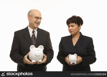 Caucasian middle-aged businessman and Filipino businesswoman holding different sized piggybanks.