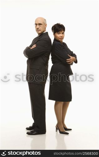 Caucasian middle-aged businessman and Filipino businesswoman standing back to back with arms crossed looking serious.