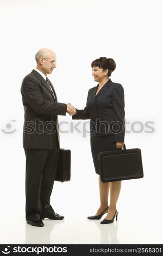 Caucasian middle-aged businessman and Filipino businesswoman standing looking at eachother shaking hands against white background.