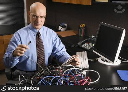 Caucasian middle-aged businessman at desk in office with a tangle of computer cables.