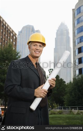 Caucasian middle aged businessman holding blueprints wearing hard hat.