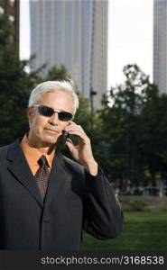 Caucasian middle aged businessman in sunglasses holding cell phone outdoors.