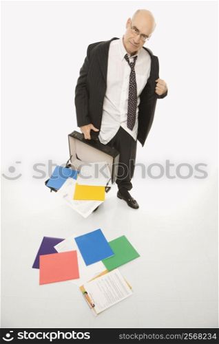 Caucasian middle-aged businessman looking disheveled holding open briefcase with papers falling out.