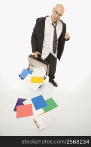 Caucasian middle-aged businessman looking disheveled holding open briefcase with papers falling out.