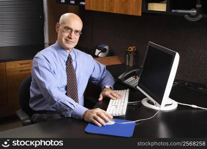 Caucasian middle-aged businessman sitting at desk in office in front of computer.