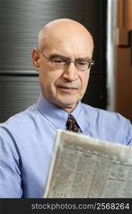 Caucasian middle-aged businessman sitting in office reading newspaper.