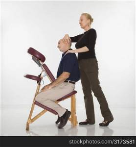 Caucasian middle-aged female massage therapist massaging neck of Caucasian middle-aged man sitting in massage chair.