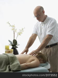 Caucasian middle-aged male massage therapist massaging back of Caucasian middle-aged woman lying on massage table.