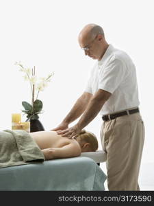 Caucasian middle-aged male massage therapist massaging back of Caucasian middle-aged woman lying on massage table.