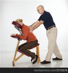 Caucasian middle-aged male massage therapist massaging back of Caucasian middle-aged woman sitting in massage chair.