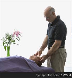 Caucasian middle-aged male massage therapist massaging face of Caucasian middle-aged woman lying on massage table.