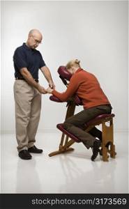 Caucasian middle-aged male massage therapist massaging hands of Caucasian middle-aged woman sitting in massage chair.
