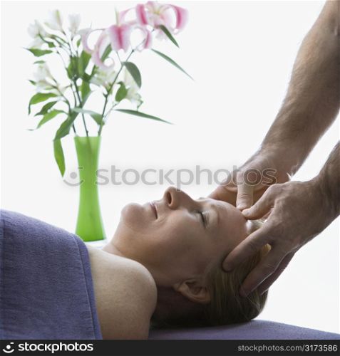 Caucasian middle-aged male massage therapist massaging temples of Caucasian middle-aged woman lying on massage table.