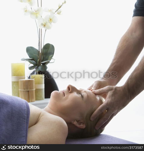 Caucasian middle-aged male massage therapist massaging temples of Caucasian middle-aged woman lying on massage table.