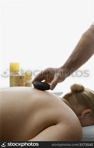 Caucasian middle-aged male massage therapist placing hot stone on back of Caucasian middle-aged woman lying on massage table.
