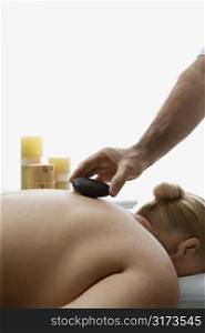 Caucasian middle-aged male massage therapist placing hot stone on back of Caucasian middle-aged woman lying on massage table.