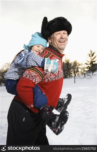 Caucasian middle aged man holding Caucasian litte girl piggyback style smiling and looking at viewer smiling.
