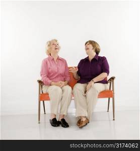 Caucasian middle aged woman and senior woman sitting and laughing.