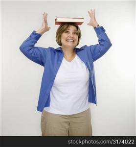 Caucasian middle aged woman balancing book on head.