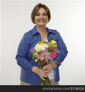 Caucasian middle aged woman holding bouquet of flowers and smiling at viewer.