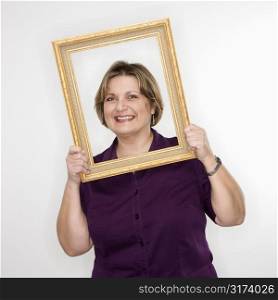 Caucasian middle aged woman holding picture frame over face.