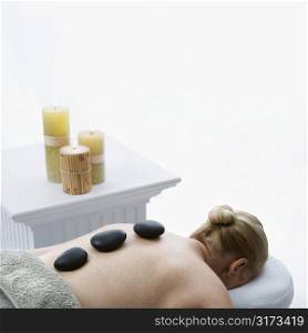 Caucasian middle-aged woman lying on massage table with hot stones on her back.