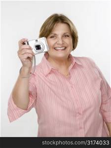 Caucasian middle aged woman taking photo with digital camera of viewer.